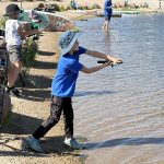 Above and below: Members of the Monument Police Department (MPD) mingled with young anglers at Monument Lake in an event called Cops and Bobbers on June 29. The event has been held elsewhere in Colorado and other states, but this was Monument’s first shot at it. The hope is that it’ll become an annual event. The aim is to give kids a chance to mingle and get to know members of their local police force while fishing. The children also got to choose from various swag including a junior police officer pin with a flashing red light and an MPD slap bracelet. By the way, for those who aren’t familiar with fishing terms, a bobber is the float that suspends the bait in the water. Above: Community Resource Officer Kelly Reifle and Scheel’s Marketing Director Jacey Sharping stand behind the table filled with MPD swag. Below: One of the kids taking part in the event casts his line. Photos by Michael Weinfeld.